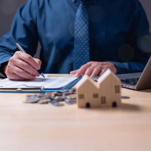 Man signing estate planning documents with a house model on the desk